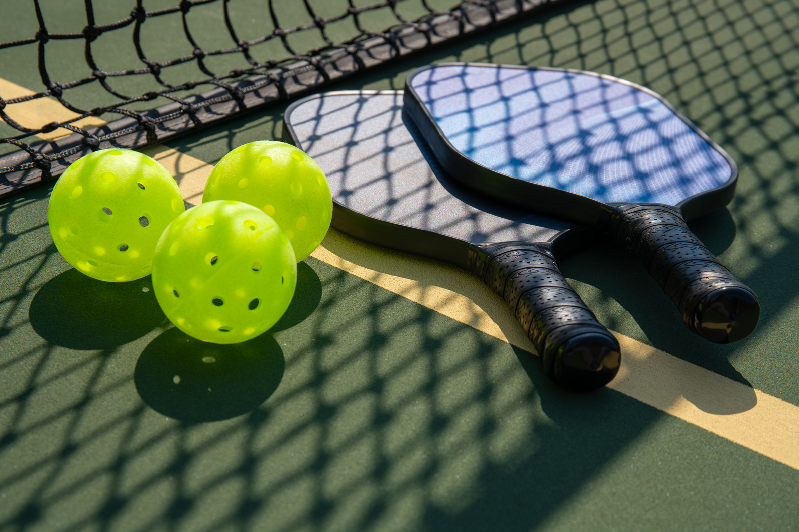 Pickleball paddles and ball in shadow of net